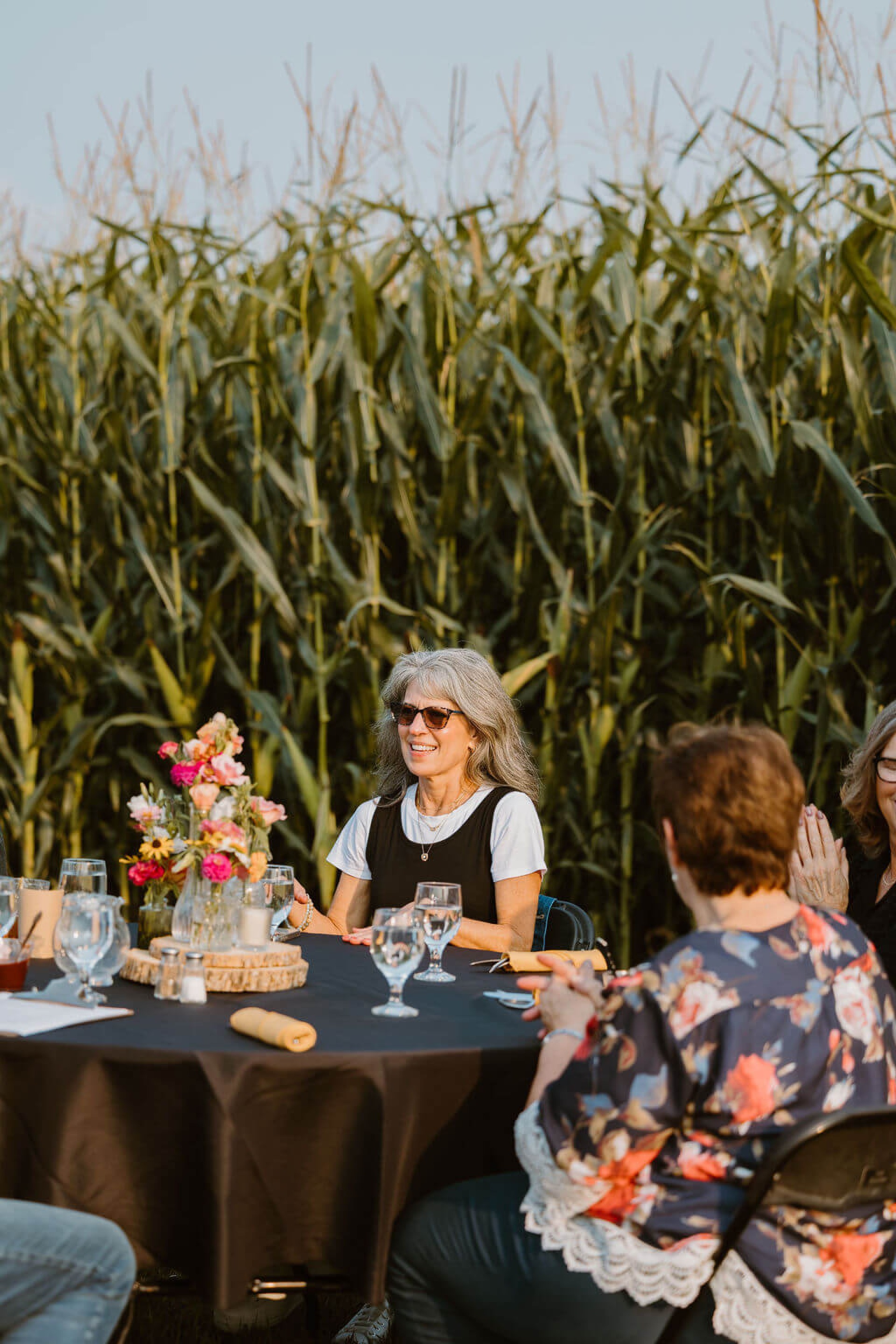 Attendees smiling at their table surrounded by corn fields at 2026 Cuisine in the Corn.