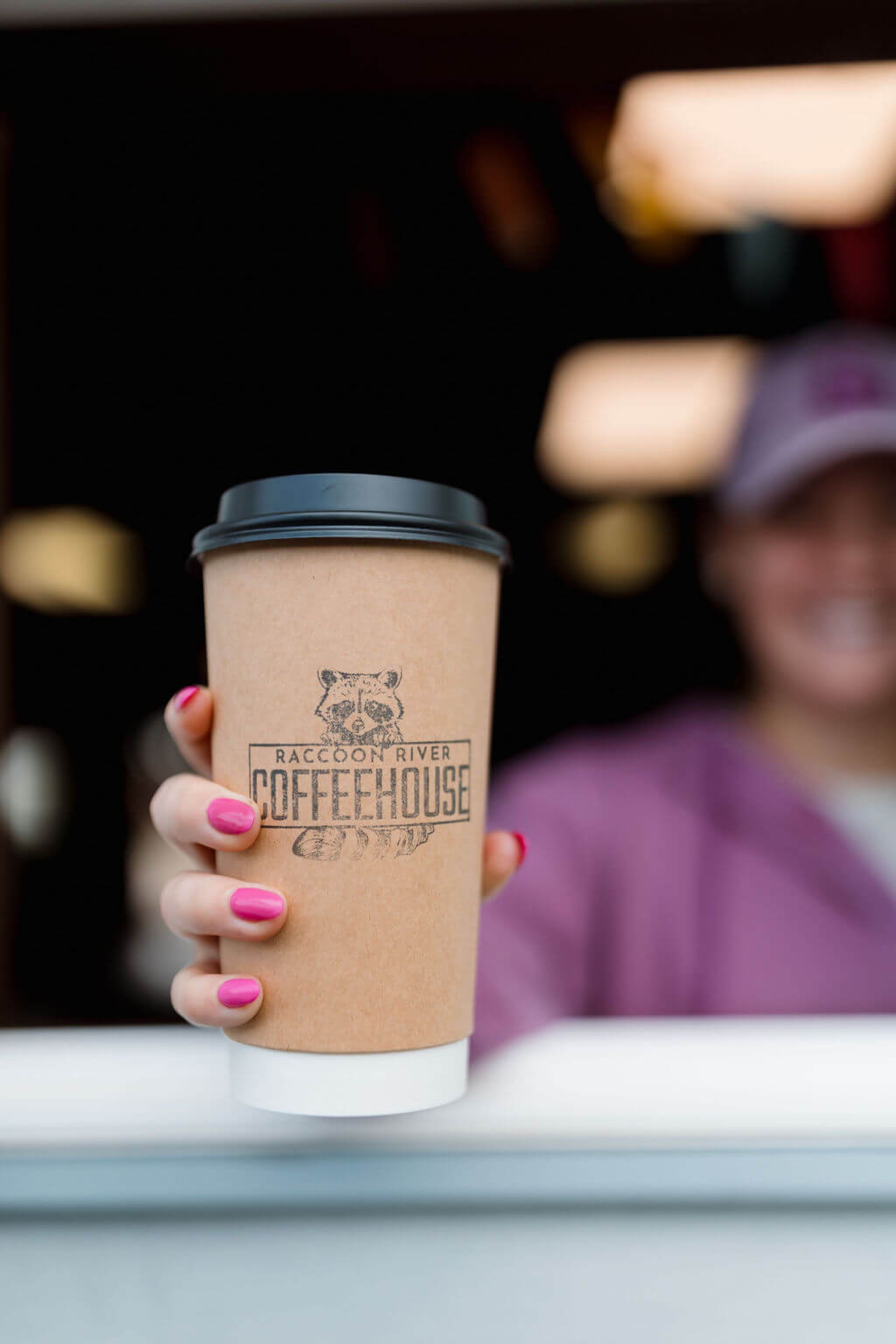 Raccoon River Coffeehouse staff member delivering a to-go coffee out the window to a waiting customer.